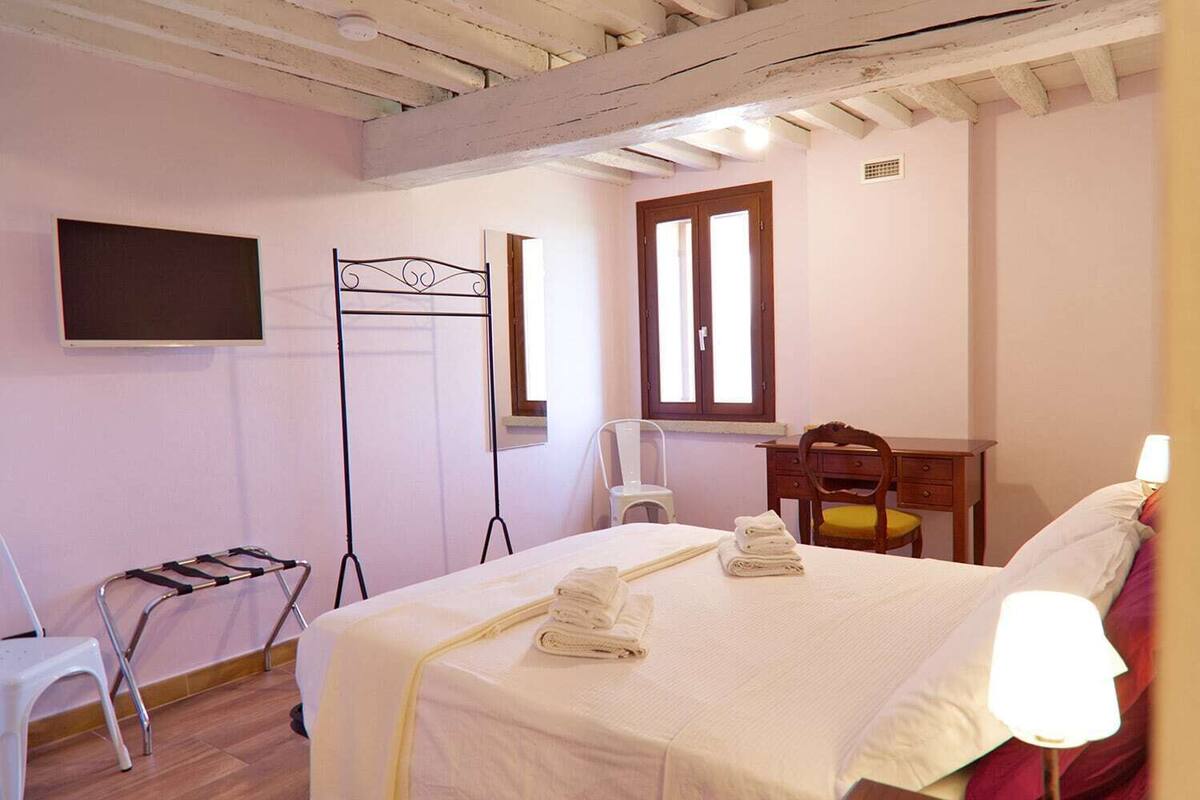 Een slaapkamer met een bed, bureau, stoel, televisie en raam.