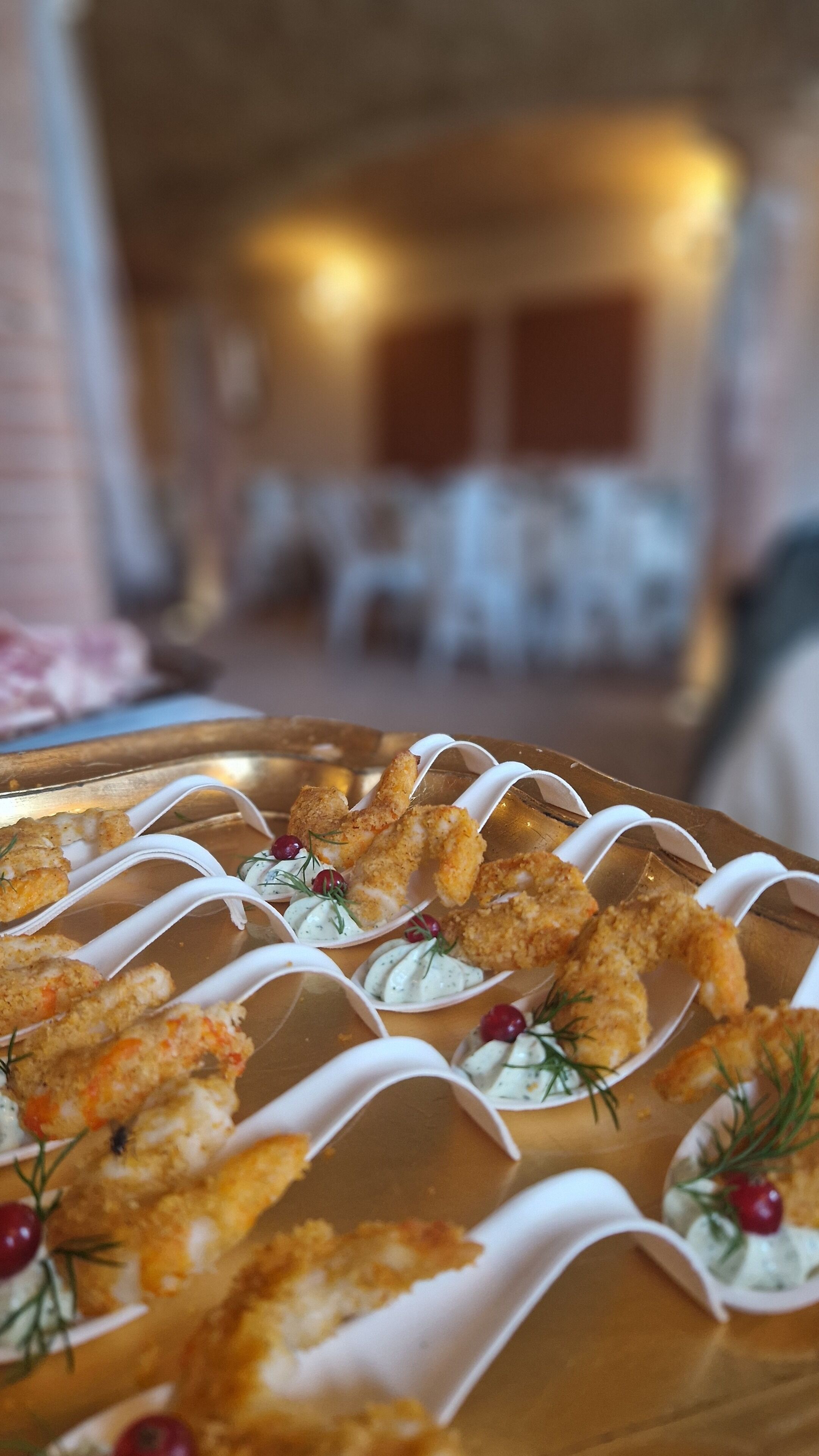 A tray of breaded shrimp appetizers on a table with a blurred background of a dining area.