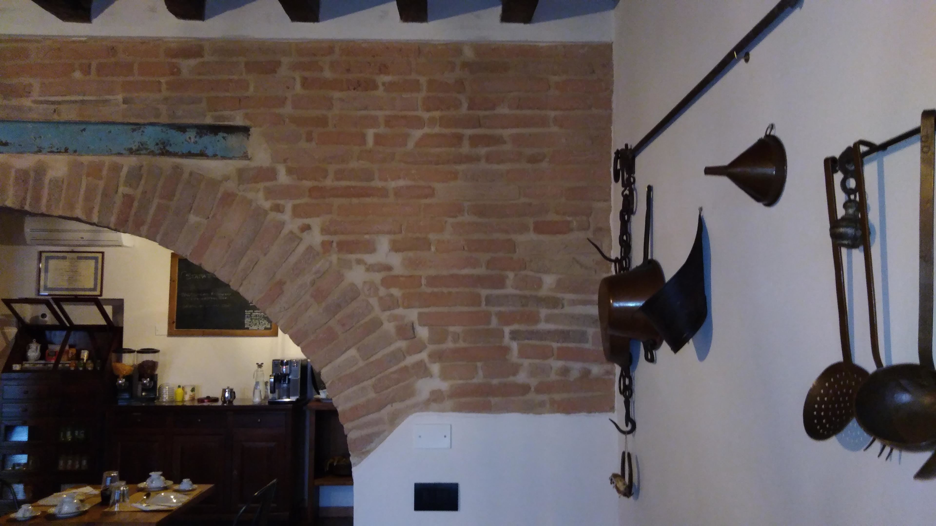 A rustic kitchen with exposed brick walls, a wooden table set for dining, and various kitchen utensils hanging on the wall.
