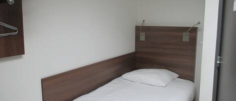 Una habitación pequeña con una cama individual, cabecera de madera, colchón blanco y aire acondicionado de pared.