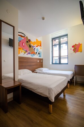 Ein Hotelzimmer mit zwei Betten, Holzboden, Wandgemälde und einem Sessel.