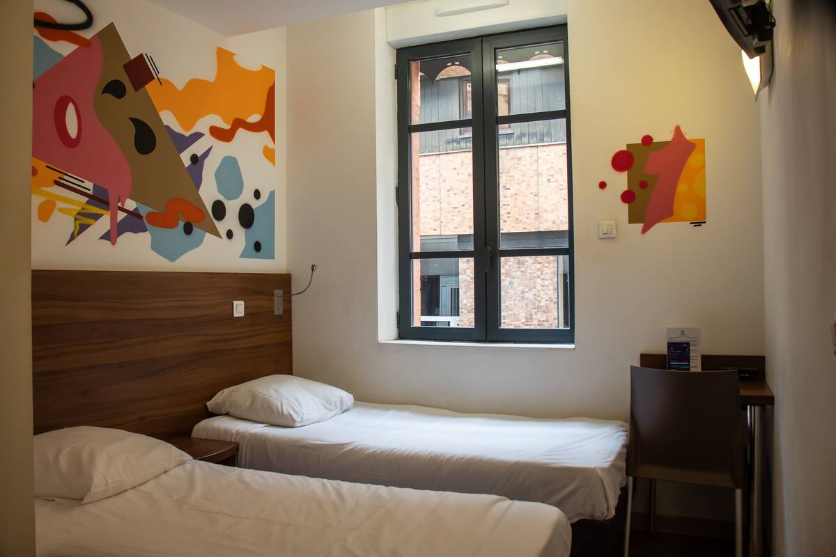A room with two beds, a window, and a wall with abstract art.