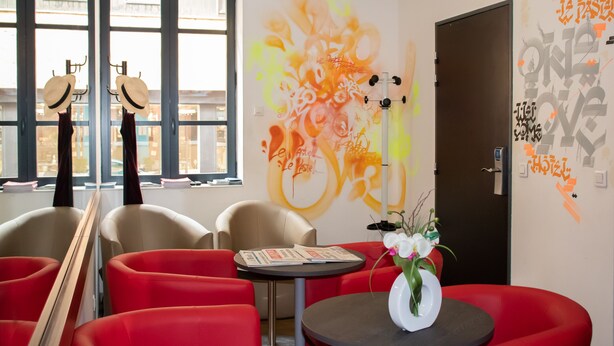 Un vestíbulo de hotel con asientos rojos, una mesa pequeña con un florero y una pared con arte abstracto y texto.