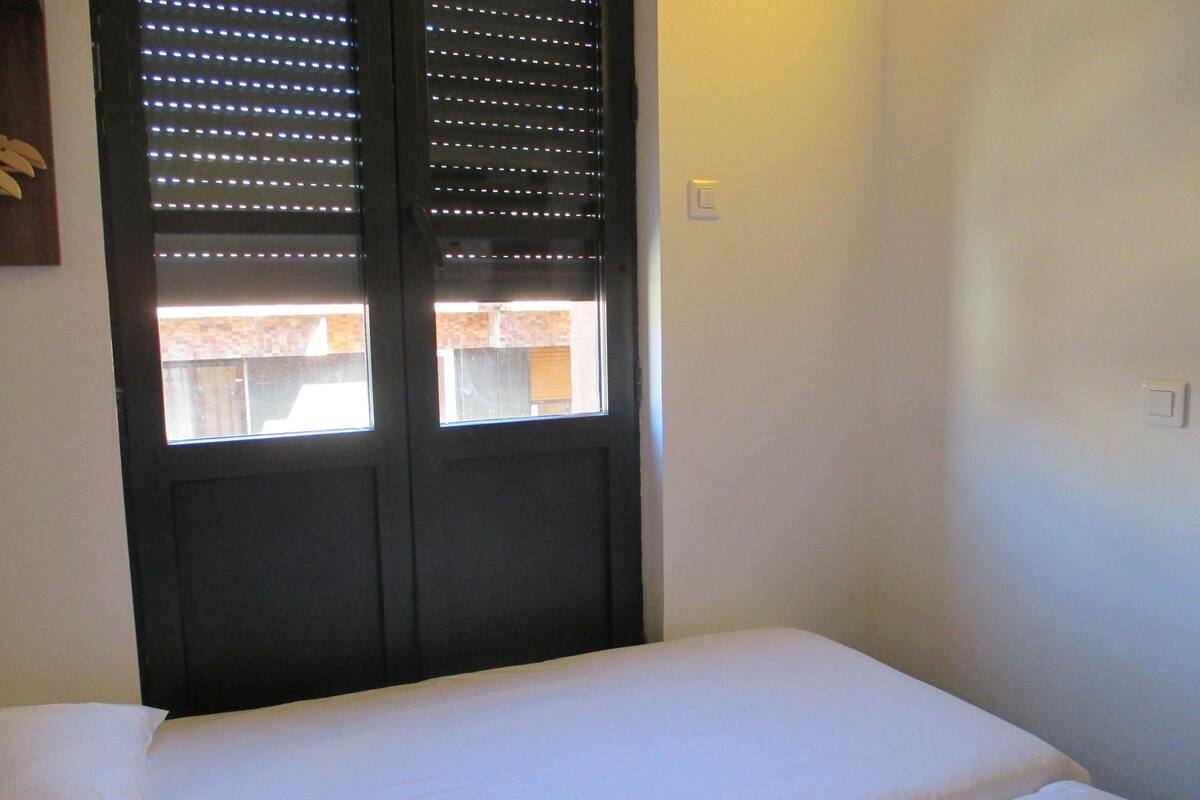 A room with a bed, a window with blinds, and a light switch on the wall.