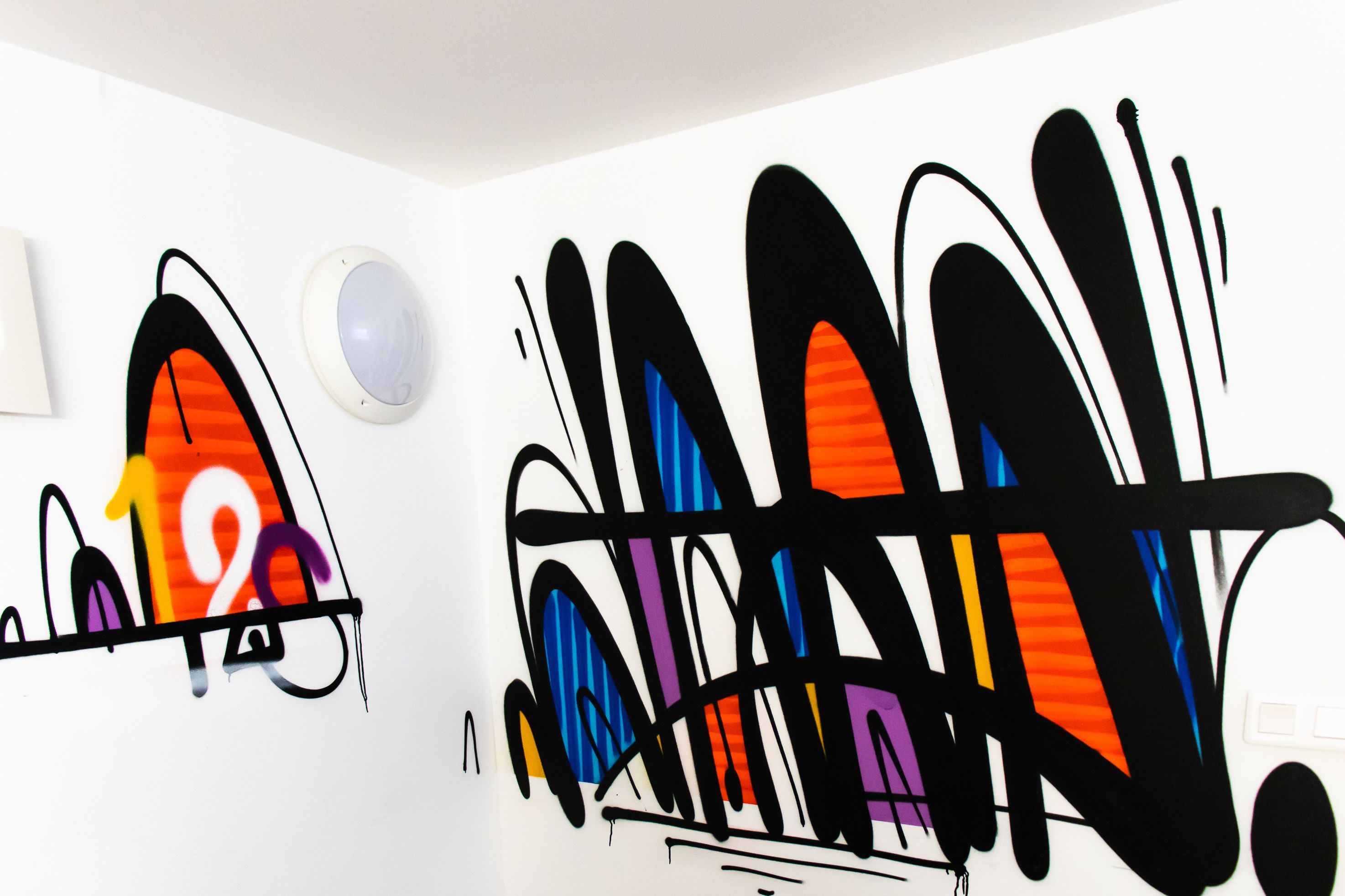Una habitación con grafitis en las paredes, techo blanco y una lámpara redonda.