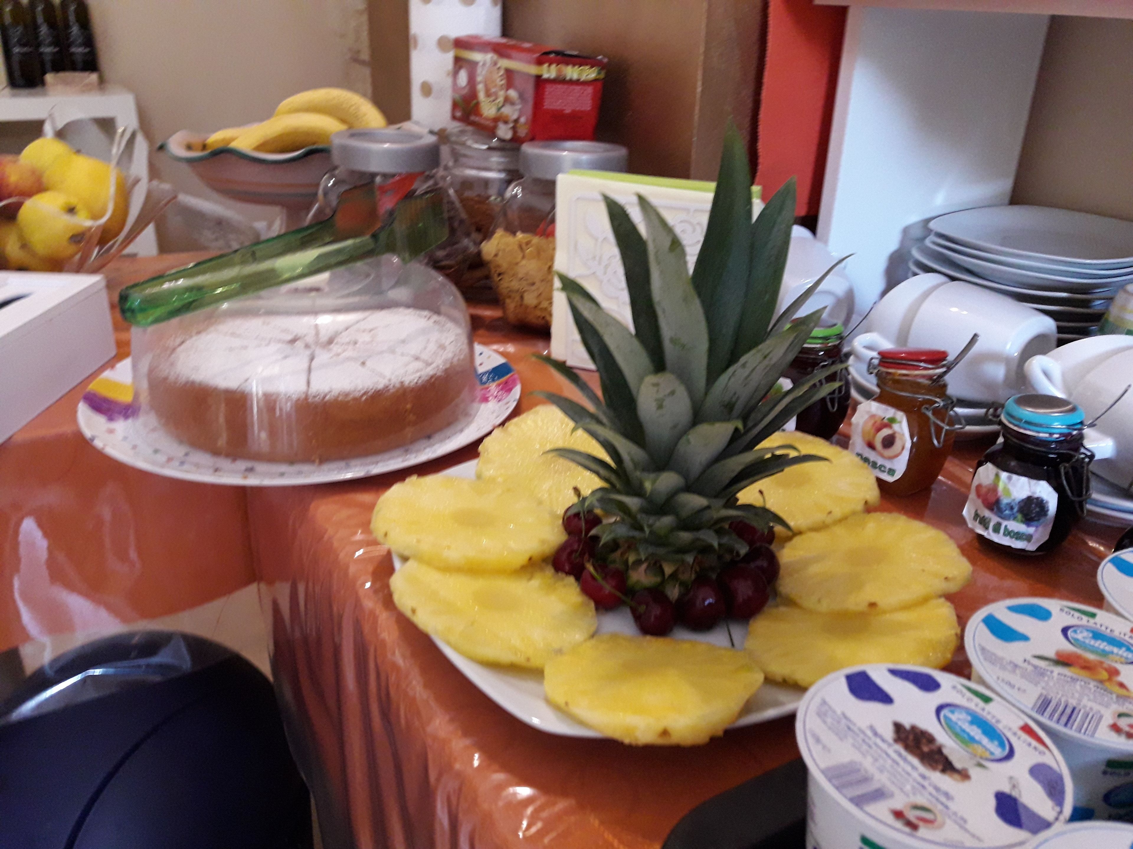 A buffet table with a covered cake, pineapple slices, and various condiments.