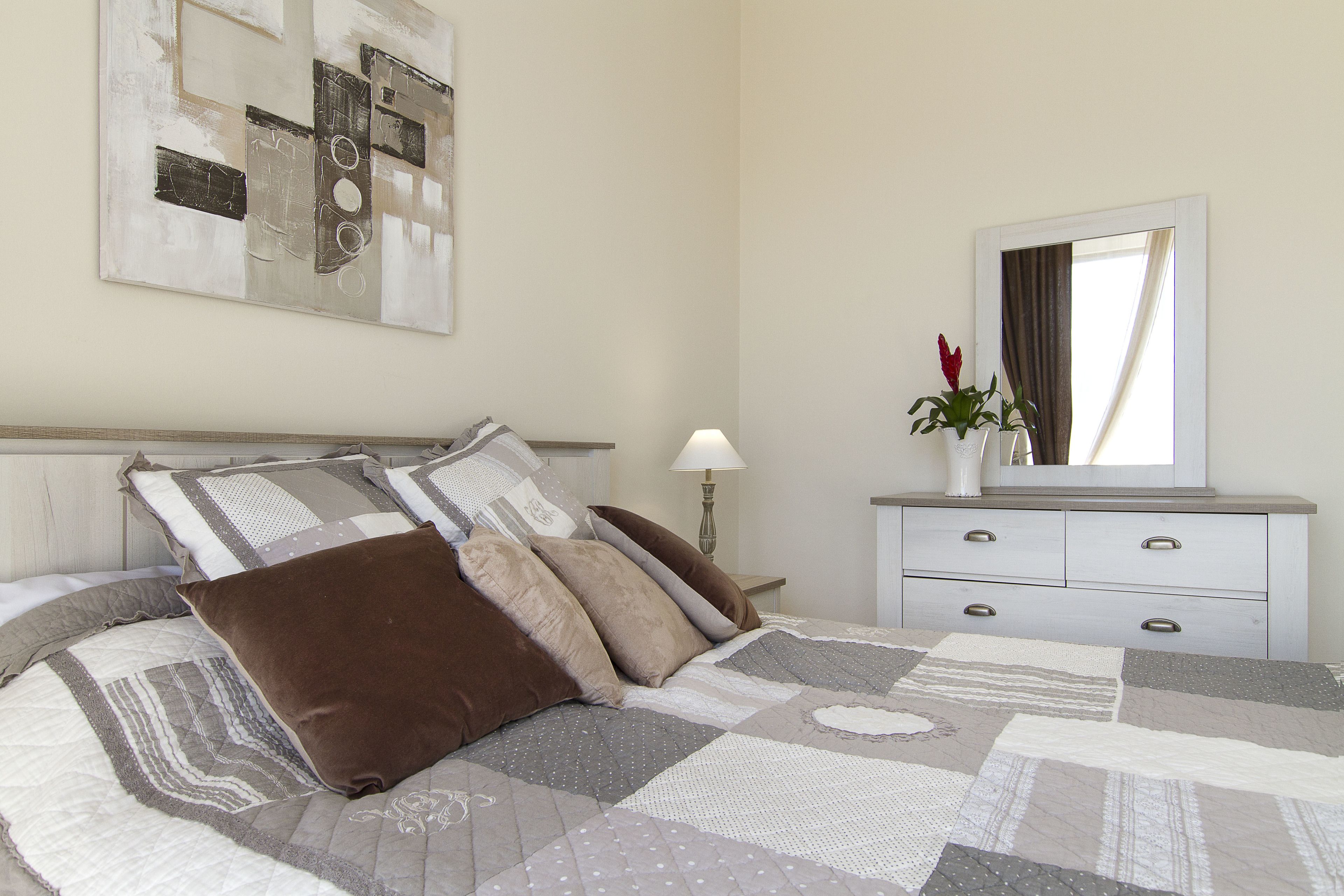 A neatly made bed with a patterned quilt, a bedside table with a lamp, and a dresser with a mirror.