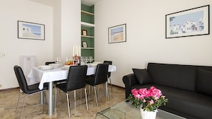 Un comedor con una mesa preparada para cuatro personas, un sofá negro y una mesa de centro de cristal con flores.