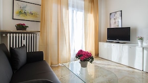 Una sala de estar con un sofá, una mesa de centro de vidrio, un televisor sobre un mueble bajo y dos cuadros en la pared.