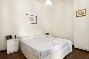 A neatly made bed with white linens and a pillow, a bedside table with a lamp and a small plant, and a framed picture on the wall. - Impero House Rent - Cavour (Stresa)