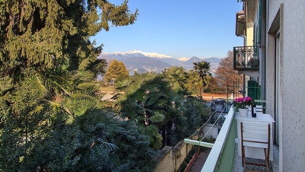 Un balcón con vistas a montañas, barandilla blanca y una pequeña mesa con una silla.