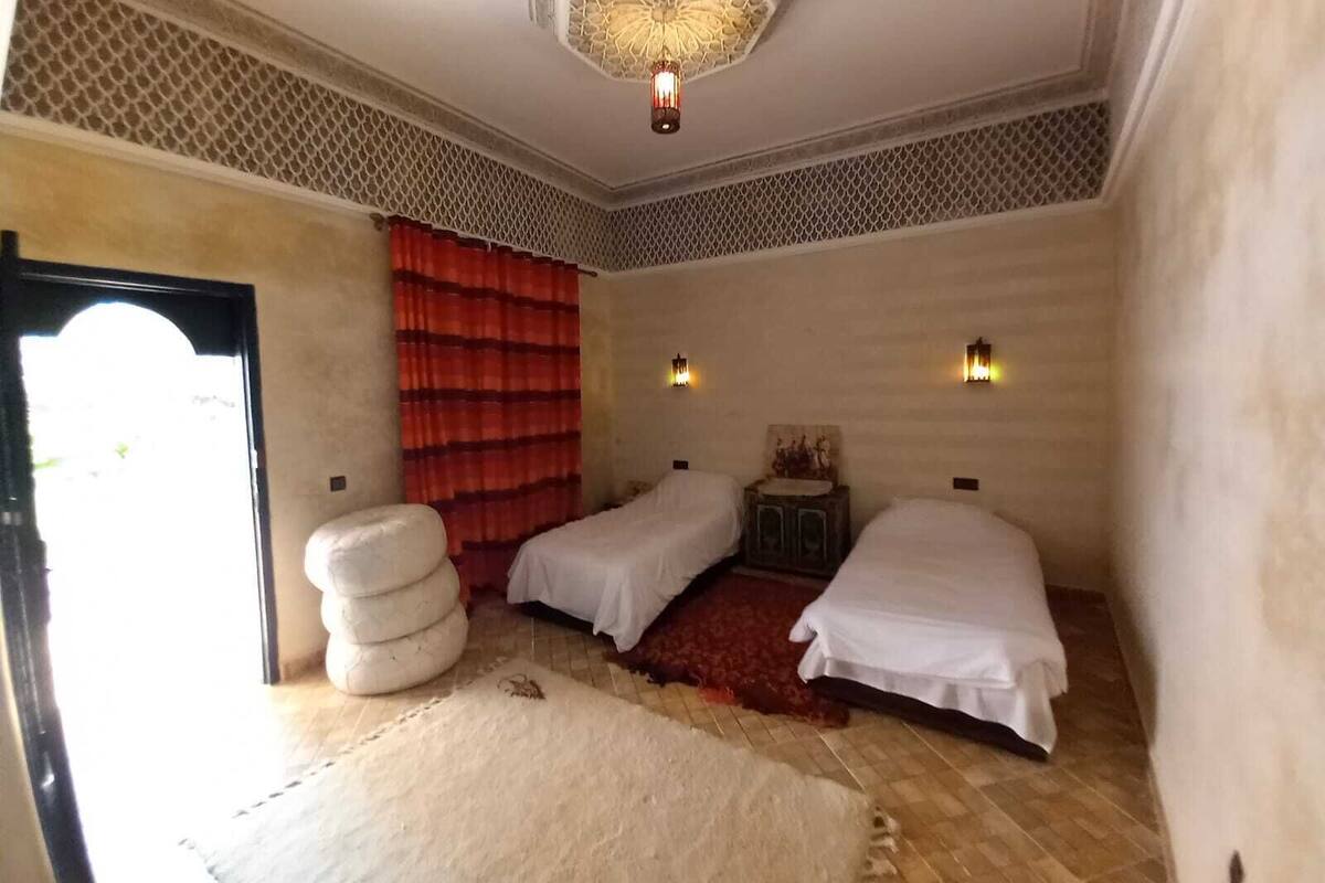 A room with two beds, a red curtain, a patterned ceiling, and a small cabinet.