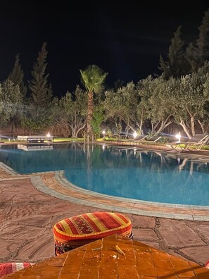 A nighttime swimming pool with a palm tree and lounge chairs.
