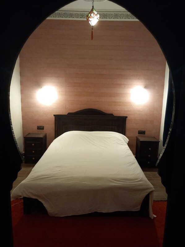 A bed with a white cover, two bedside tables, and a hanging light fixture.