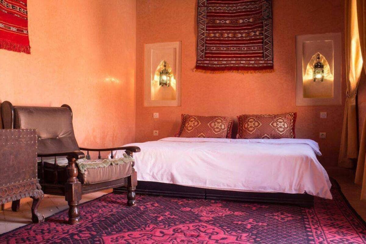 A bedroom with a bed, a chair, a patterned rug, and wall-mounted lights.