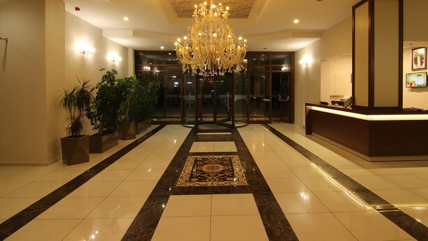 Un hall de hotel con una imponente lámpara de araña, un mostrador de recepción y plantas en macetas.