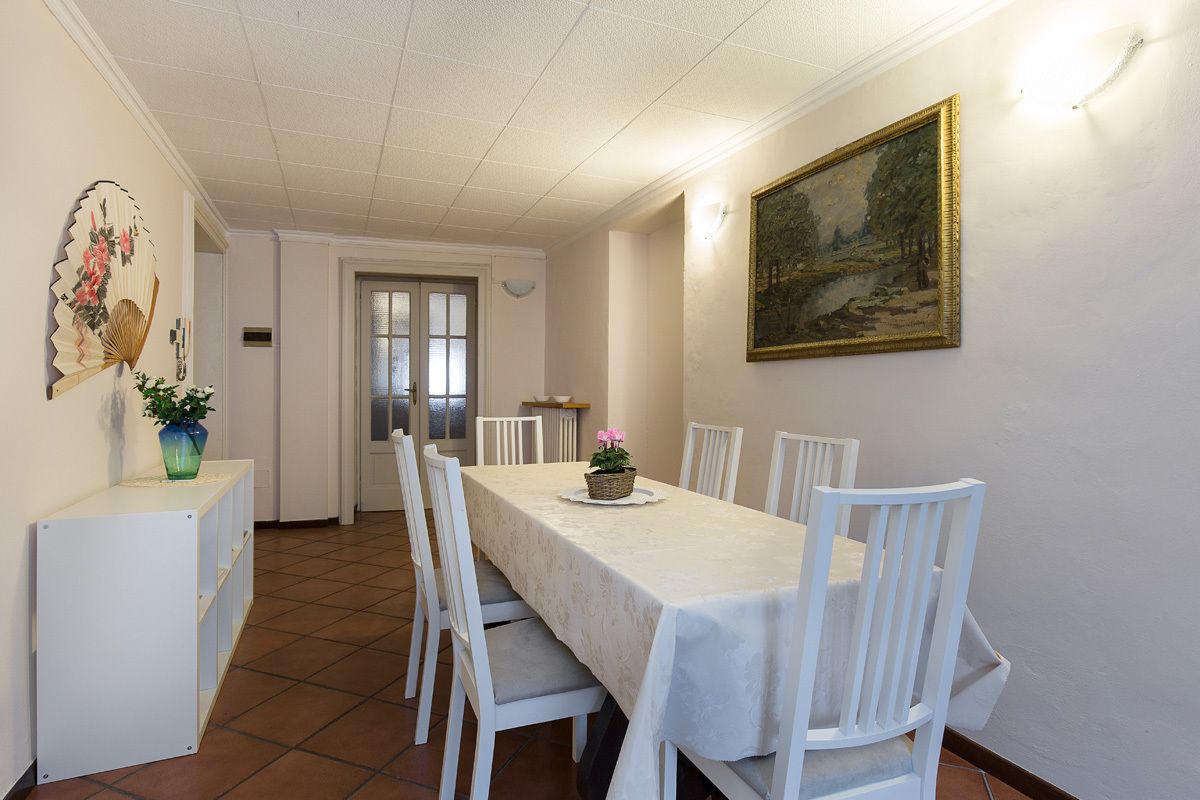 A dining area with a table set for four, white chairs, a painting on the wall, and a door leading to another room.