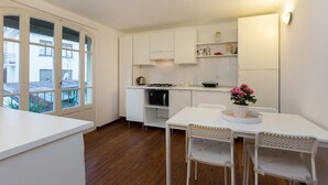 Uma cozinha moderna com armários brancos, uma mesa de jantar com cadeiras e vista para o exterior através de grandes janelas.