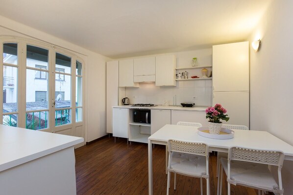 Une cuisine moderne avec des meubles blancs, une table à manger avec des chaises et une vue sur l’extérieur grâce à de grandes fenêtres.
