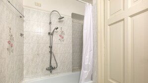 Casa de banho com banheira, chuveiro e paredes revestidas de azulejos.