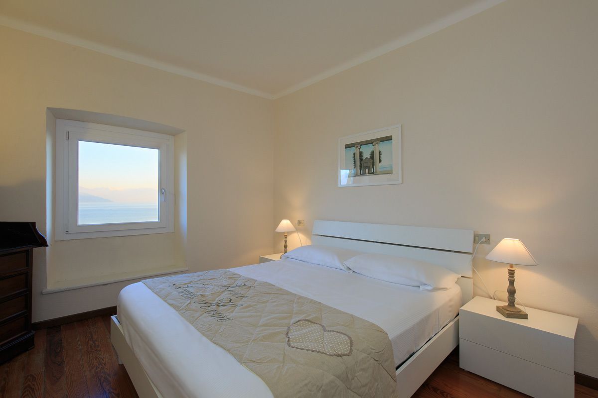 A neatly arranged bedroom with a bed, two bedside tables with lamps, a window, and a framed picture on the wall.