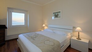 Quarto bem arrumado com uma cama, duas mesas de cabeceira com abajures, uma janela e um quadro na parede.