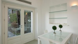 A modern dining area with a glass table, white chairs, and a small potted plant. - Impero House Rent - Maison du Lac (Baveno)