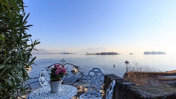 A seaside patio with a table and chairs, overlooking a calm body of water with distant landforms. - Impero House Rent - Maison du Lac (Baveno)