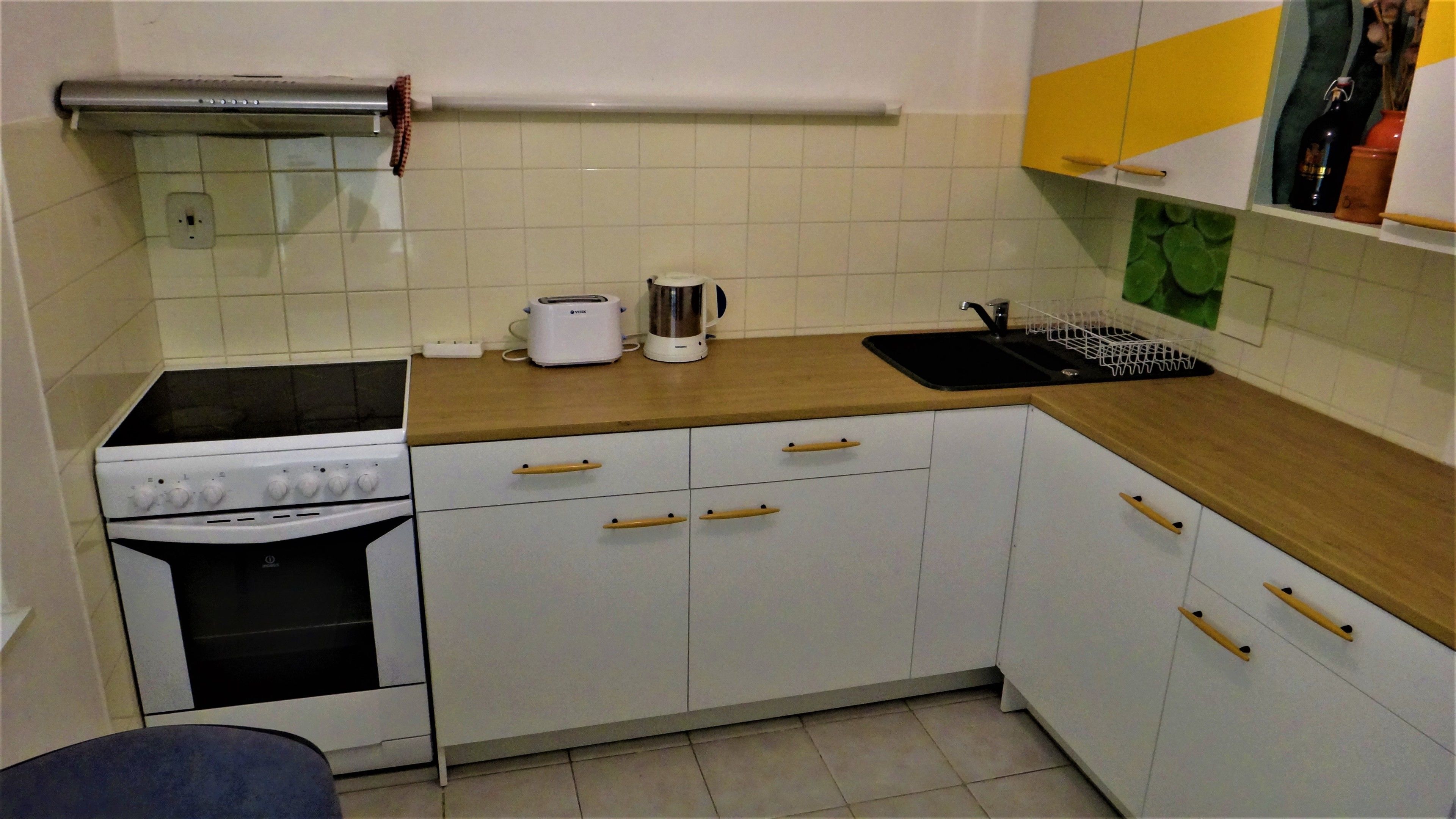 A compact kitchen with white cabinets, a stove, a toaster, and a sink.