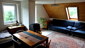 A cozy room with a wooden ceiling, a blue sofa, a dining table with a rug, and a potted plant. - Prázdninový dům Pacl (Cervená Recice)