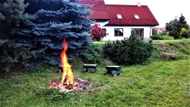 A house with a red roof, a fire in the yard, and a bench. - Prázdninový dům Pacl (Cervená Recice)