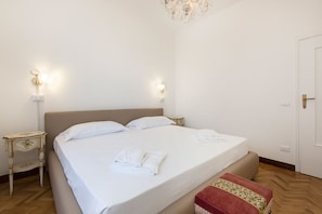 A neatly made bed with white linens and a red throw blanket, two bedside tables with wall-mounted lamps, and a wooden floor.
