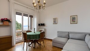 A dining area with a table, chairs, and a chandelier. There is a sofa and a window with curtains. - Impero House Rent - Rampolina View (Stresa)