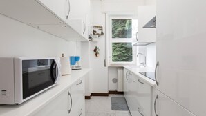 A modern kitchen with white cabinets, a built-in microwave, and a window with a view of greenery. - Impero House Rent - Rampolina View (Stresa)