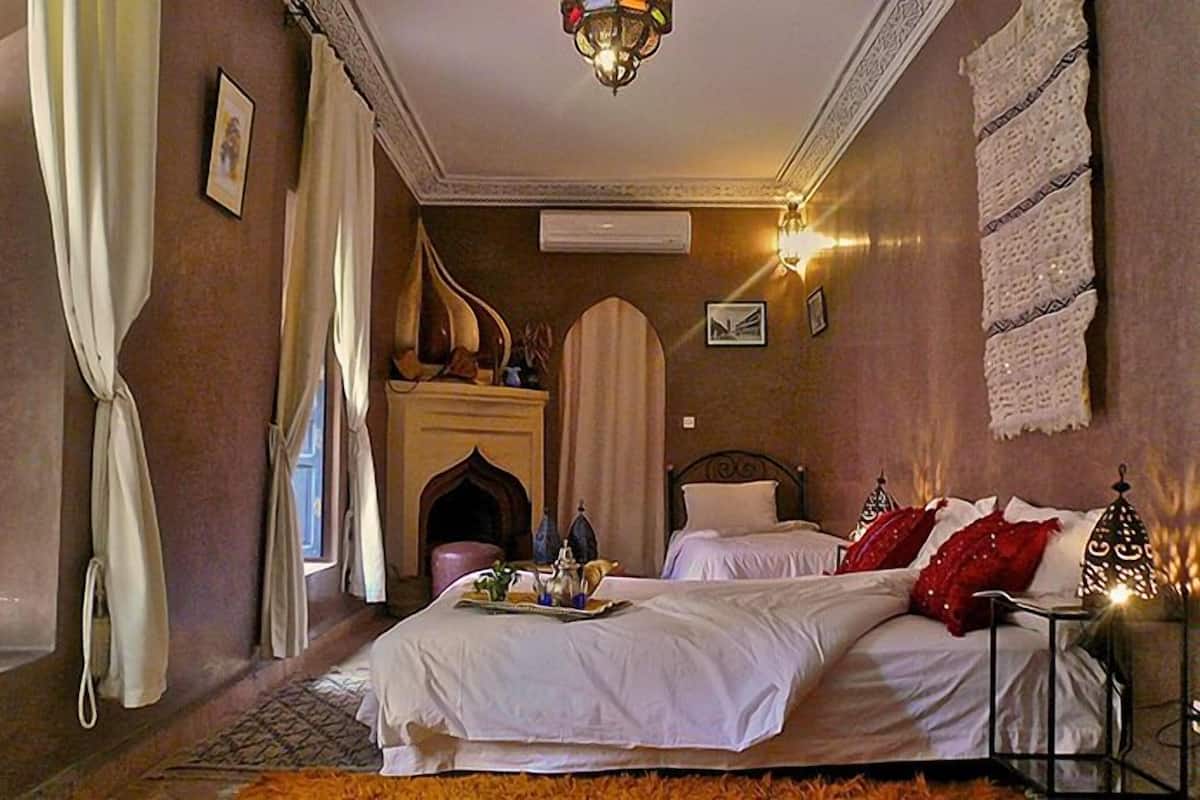 A traditional room with two beds, a fireplace, and decorative wall hangings.