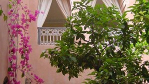 A building with pink walls, two arched windows with white curtains, and a balcony with a metal railing. - Riad Sidi Omar (Marrakech)