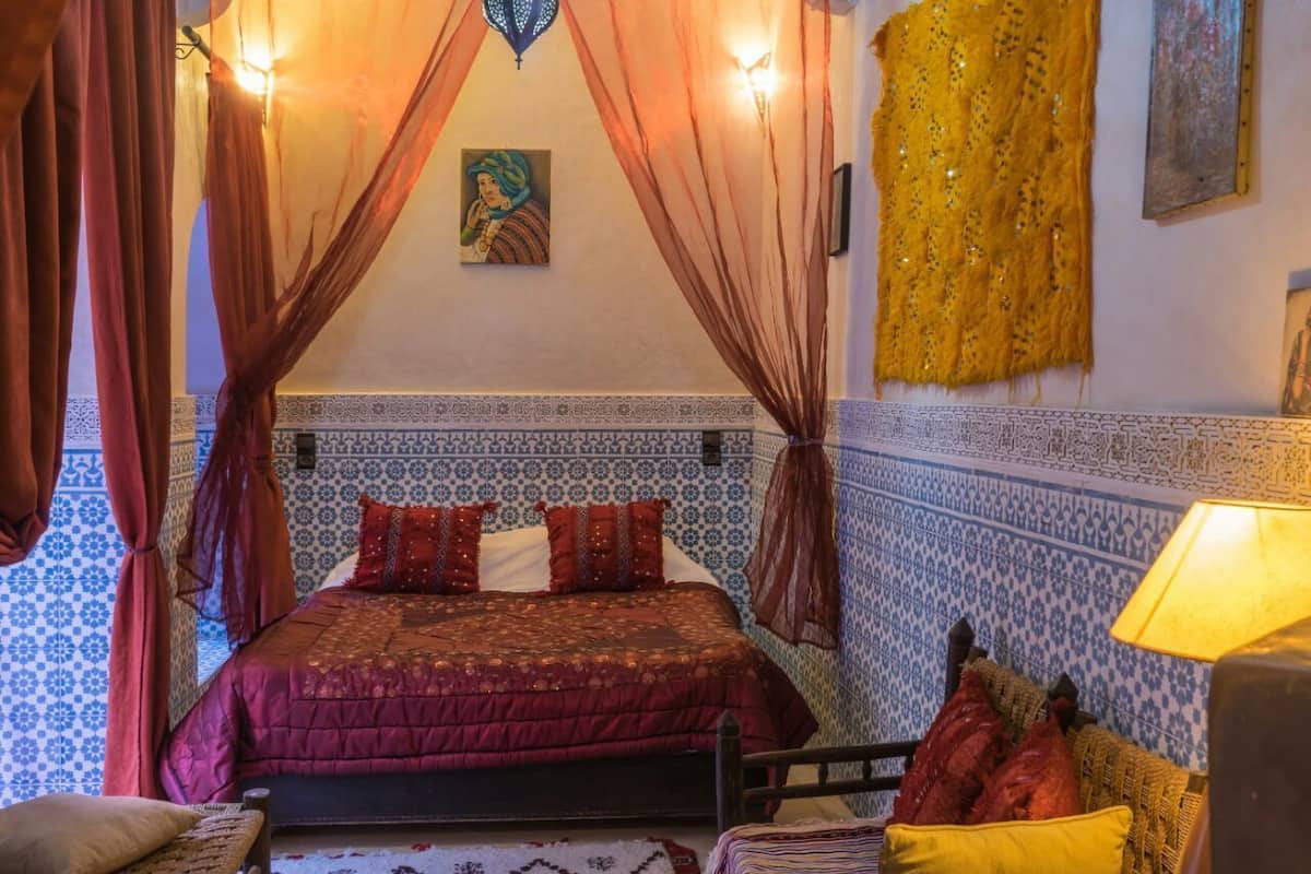 A room with a bed, curtains, a lamp, and patterned walls.