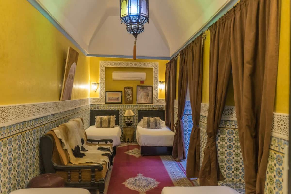 A narrow hallway with two beds, a patterned wall, a hanging lantern, and a red carpet.