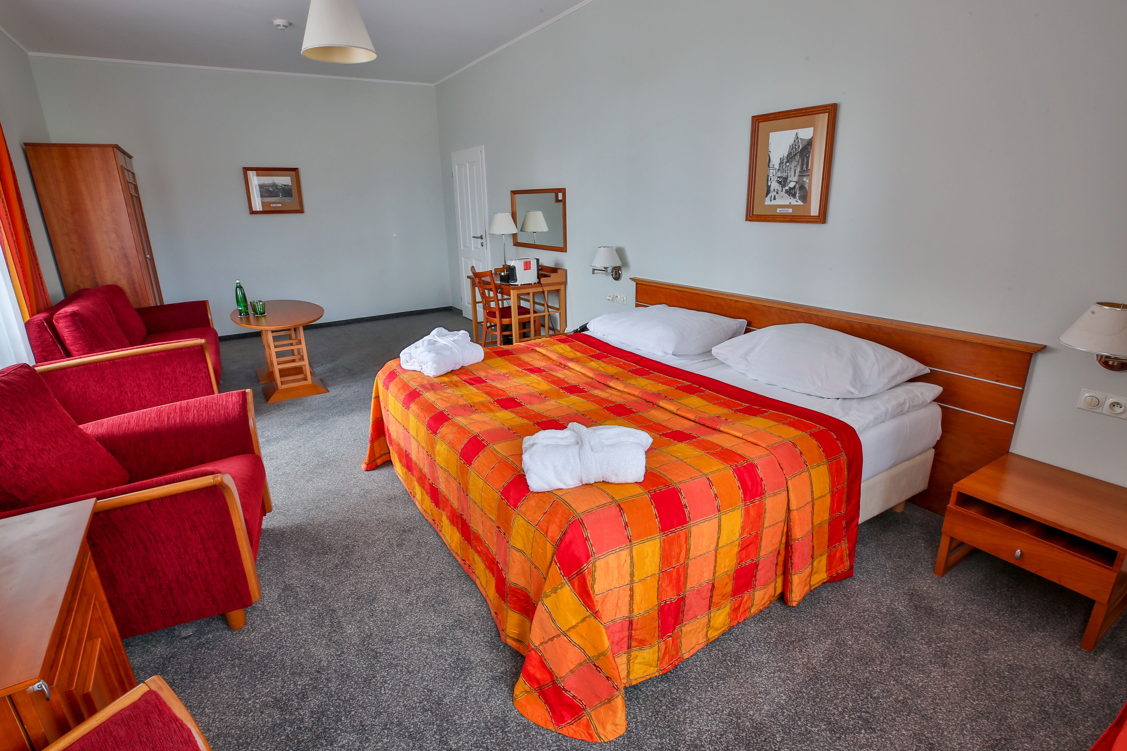 Una habitación de hotel con una cama grande, un sofá rojo, un escritorio de madera y una silla.