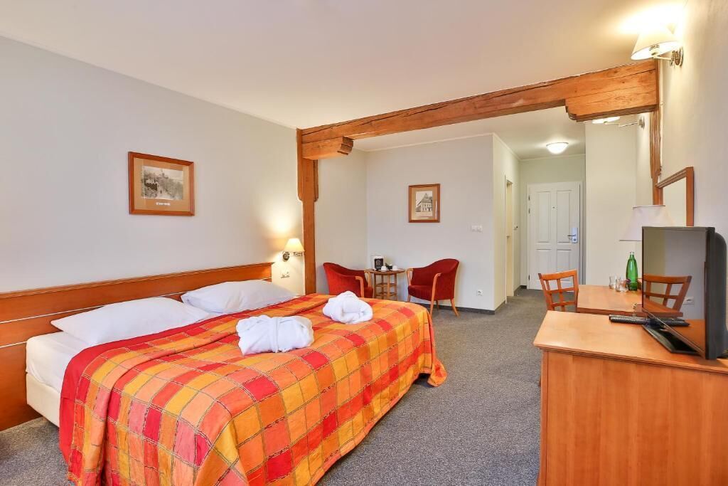 A hotel room with a bed, a desk, a chair, and a television.