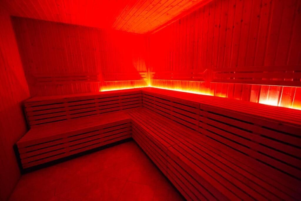 A sauna room with wooden benches and a red-lit ambiance.