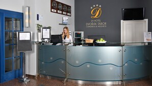 A reception desk with a woman behind it, a wall clock, a television, and a sign for LH Hotel Dvorak Tabor Congress & Wellness. - LH Hotel Dvorak Tabor (Tabor)