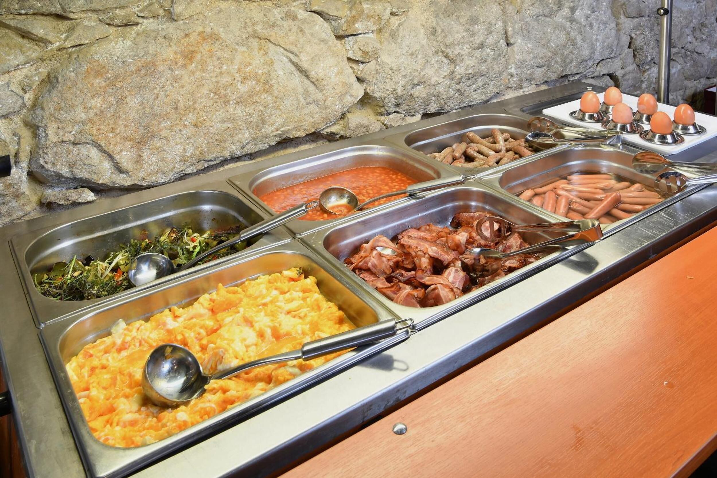 Un buffet proposant une variété de plats, notamment des haricots, des saucisses et une salade.