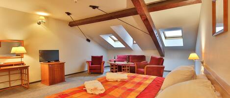 A hotel room with a bed, a desk, a TV, a chair, a table, and two skylights.