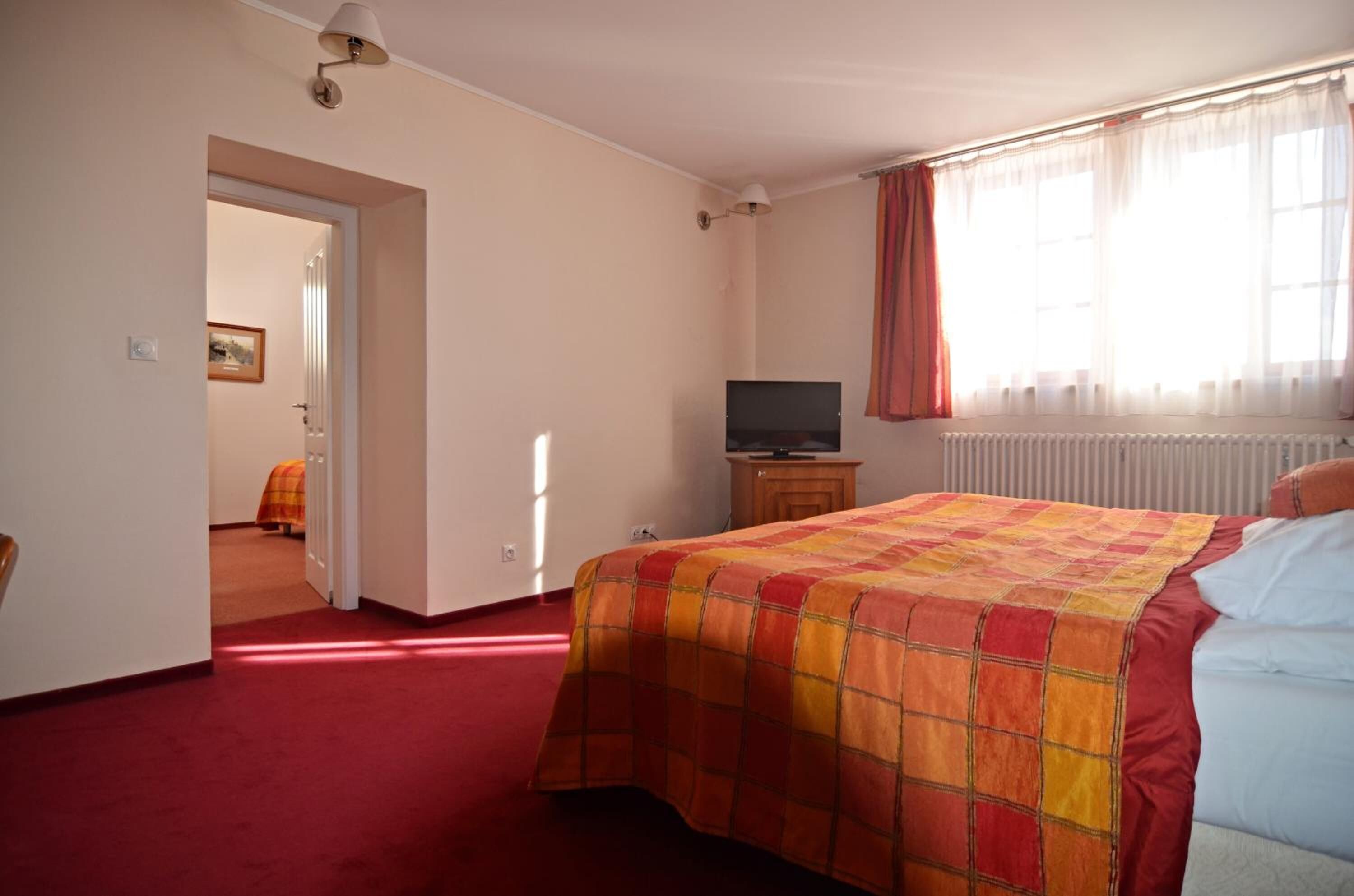 A bedroom with a bed, a television, a radiator, and a door leading to another room.