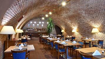 Un restaurante con arcos de ladrillo, mesas de madera, sillas con cojines azules y una zona de bar al fondo.