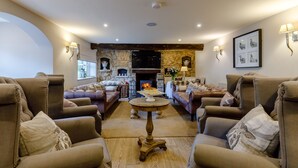 A spacious living room with leather armchairs, a round wooden coffee table, and a stone fireplace. - The Grousemoor Country House (Wrexham)