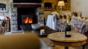A cozy room with a fireplace, a round wooden table with a bottle of champagne and glasses, and a comfortable seating area. - The Grousemoor Country House (Wrexham)