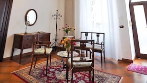 Una habitación con techo alto y decorado, muebles de madera y un ventanal con cortinas.