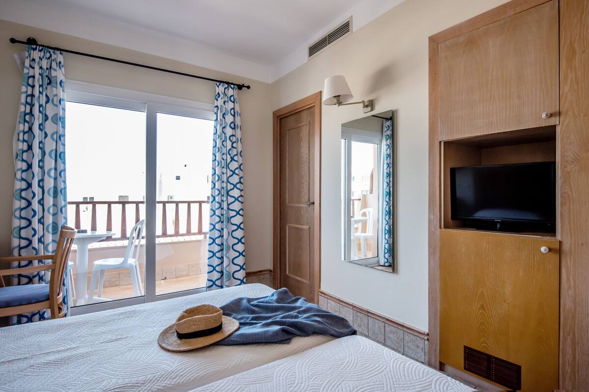 Ein Hotelzimmer mit Bett, Fernseher, Balkon mit Stühlen und Holzschrank.